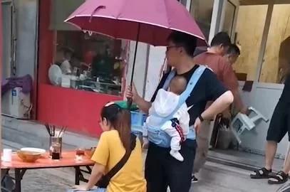 妻子雨中吃面丈夫身旁打伞,身上还背着孩子